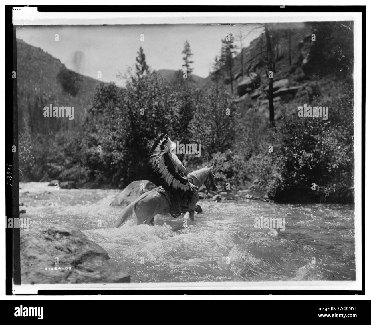 Bullchief alla ford, c1905. Bullchief, che indossa il cofano da guerra, attraversa rapide poco profonde a cavallo. Foto Stock