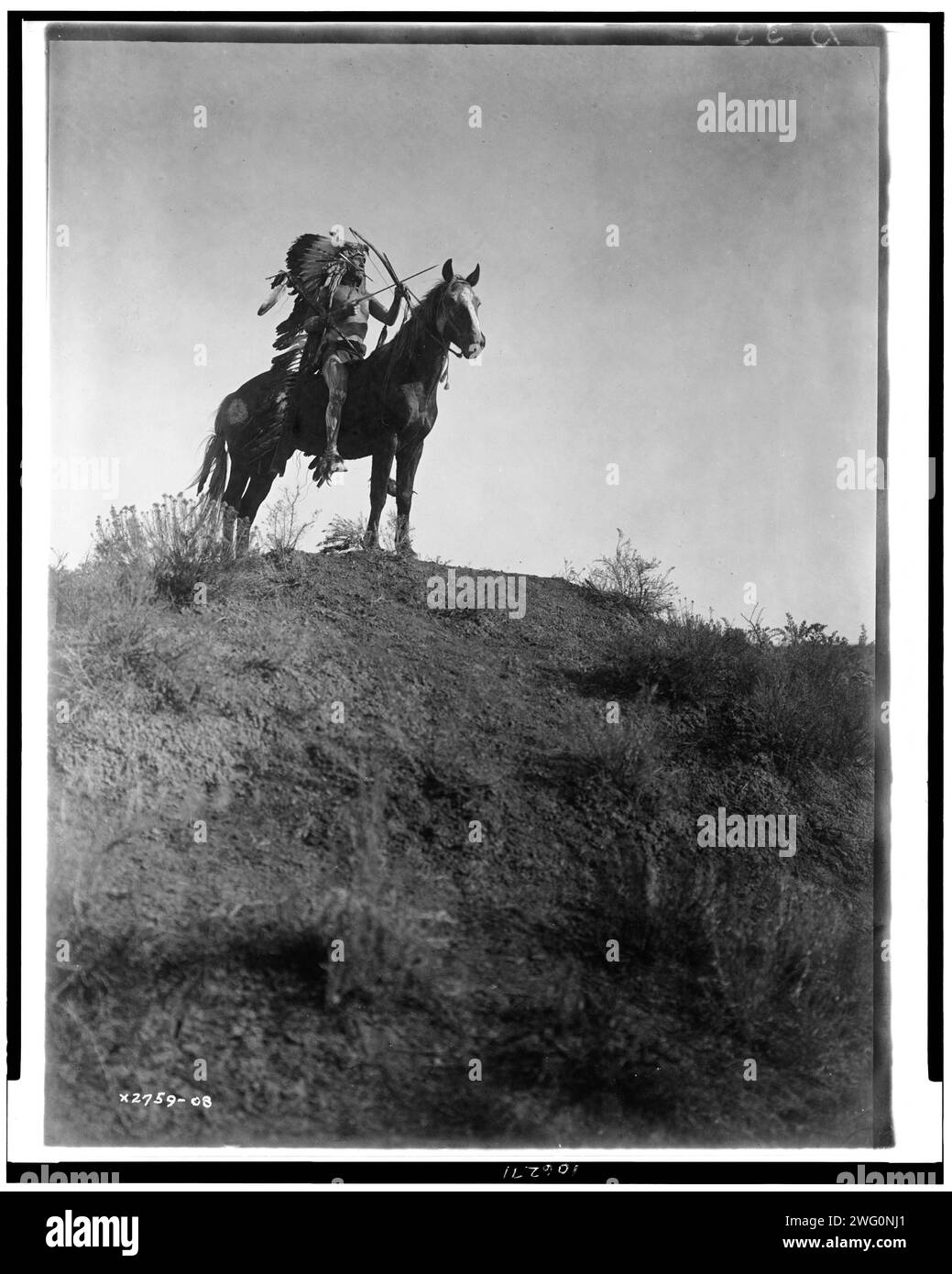 Pronto per l'accusa-Apsaroke, c1908. Uomo con copricapo di piume, a cavallo, con arco e frecce, 1 freccia in bocca. Foto Stock