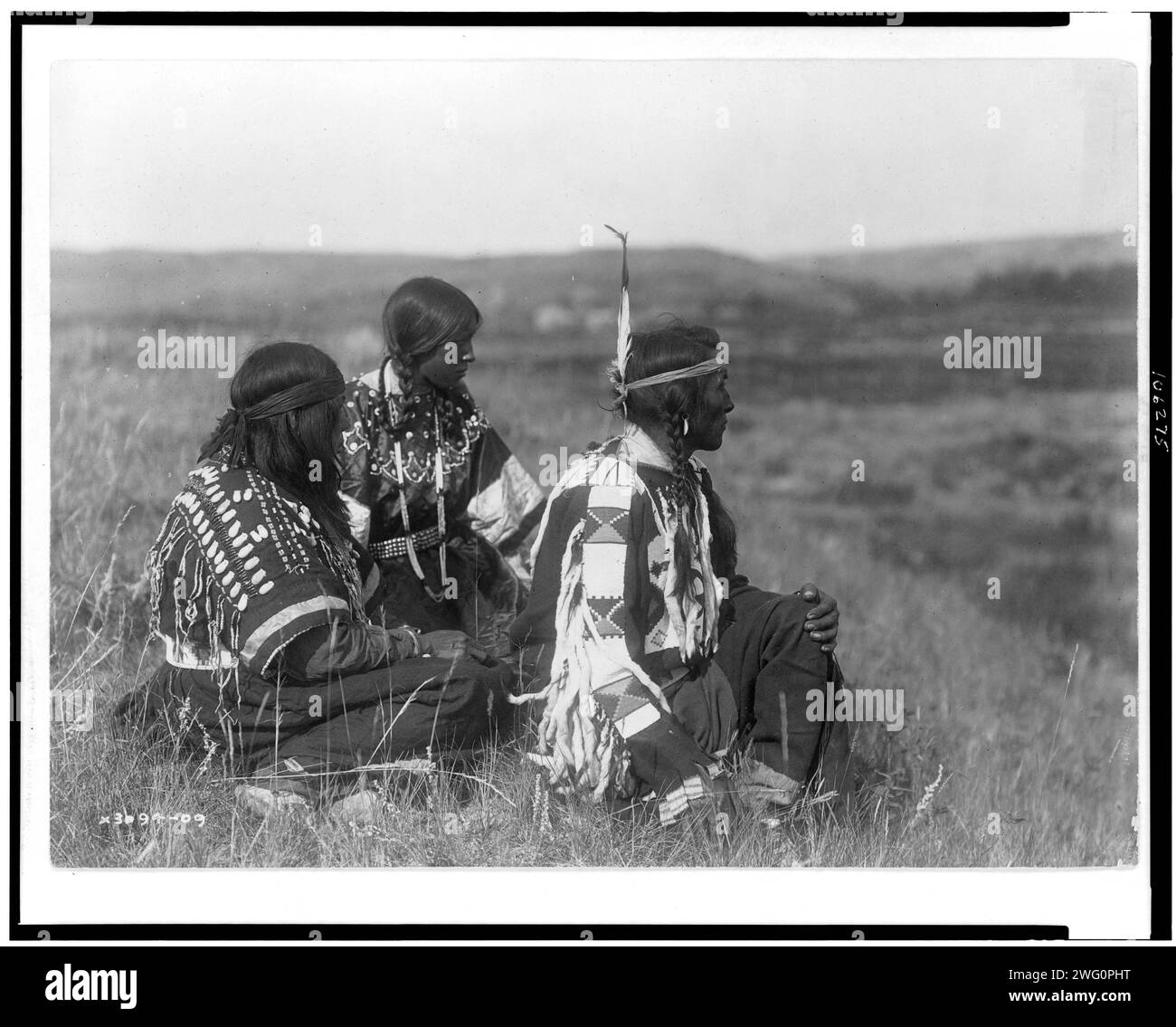Affacciato sul campo Piegan, c1910. Un uomo e due donne, seduti sulla collina, rivolti a destra. Foto Stock