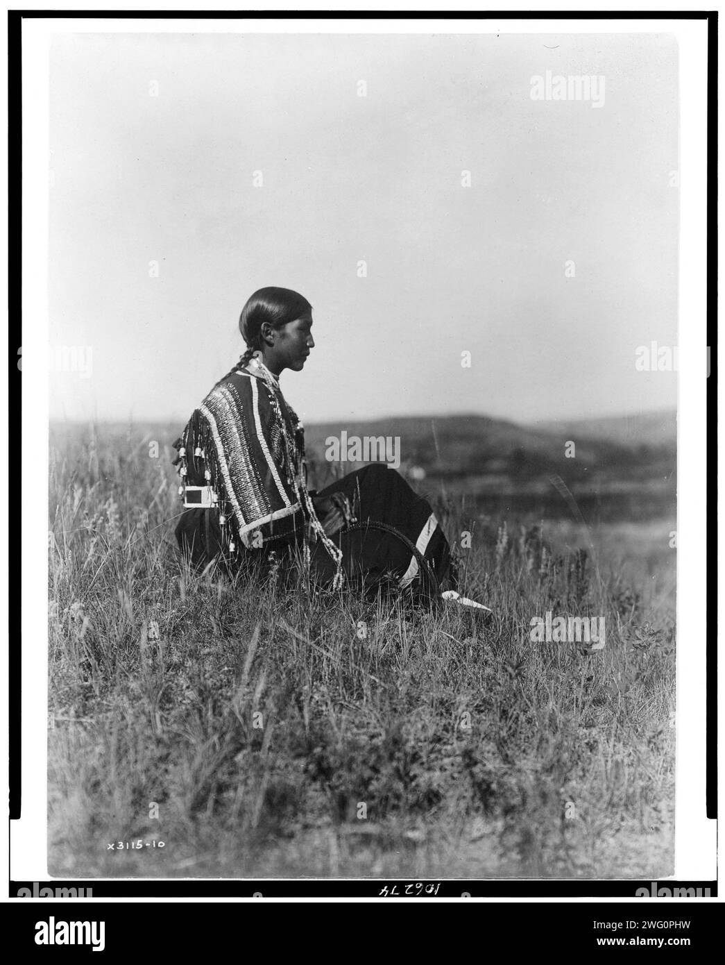 Day Dreams-Piegan, c1910. Giovane donna indiana Piegan, con vestito in perline, seduta sulla collina. Foto Stock