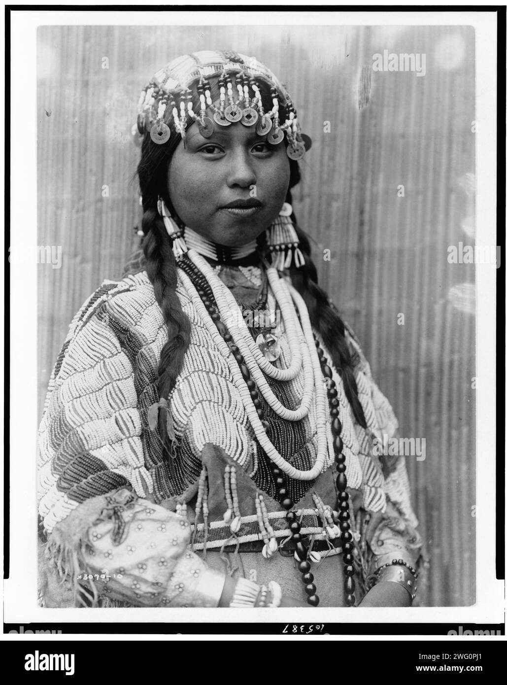 Sposa Wishham, c1910. Sposa Tlakluit, ritratto a mezza lunghezza, rivolto leggermente a destra, con trecce, copricapo con perline con monete cinesi, orecchini con conchiglia dentalica, abito in pelle di sarca con perline, perline intorno al collo. Foto Stock