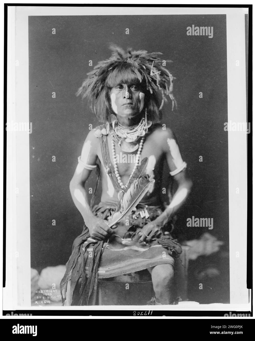 Prete serpente Honovi-Walpi, con dipinto Totkya Day, c1910. Hopi Snake Priest, ritratto lungo tre quarti, seduto, rivolto verso la parte anteriore. Foto Stock
