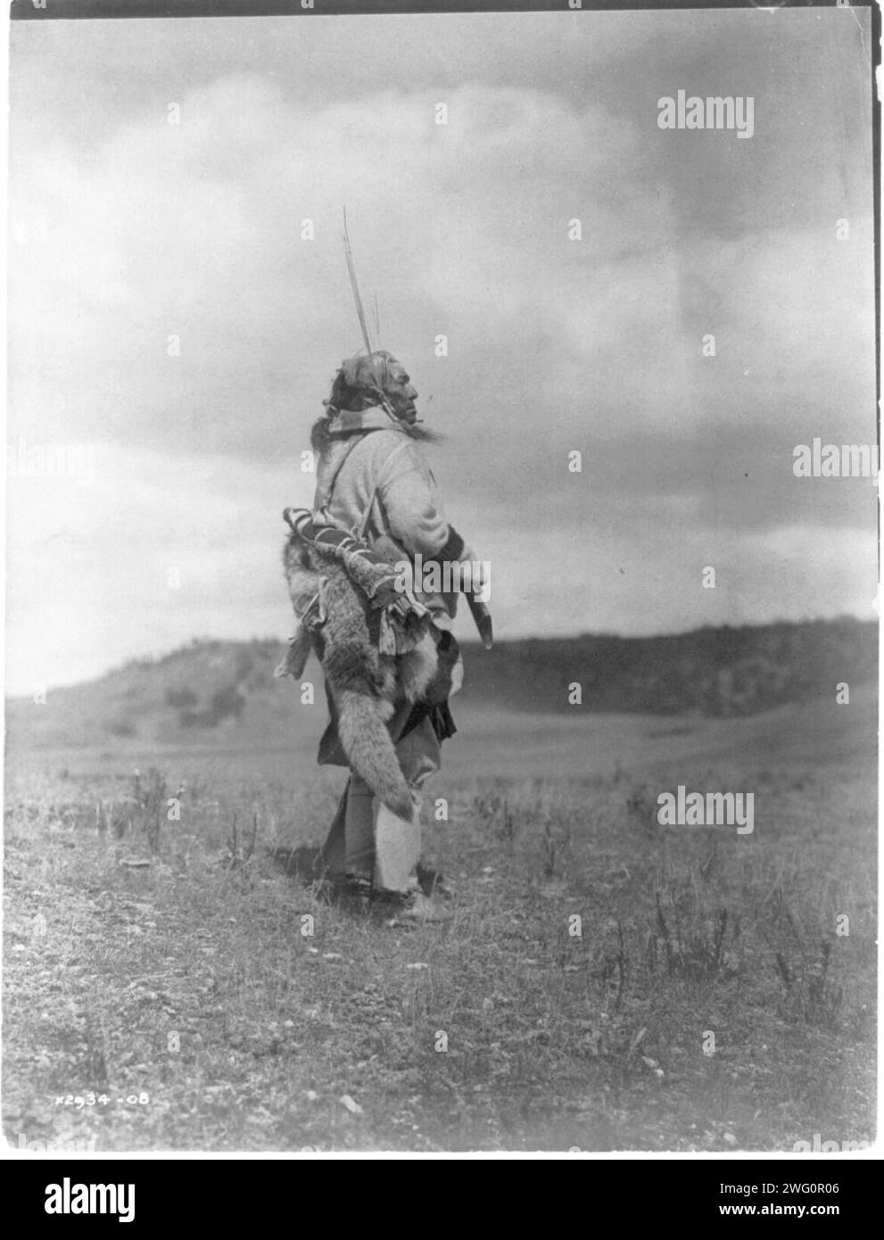 Lo scout-Atsina, c1908. Atsina uomo, ritratto a tutta lunghezza, in piedi, girò a destra, tenendo il fucile mentre guardava su una pianura erbosa. Foto Stock