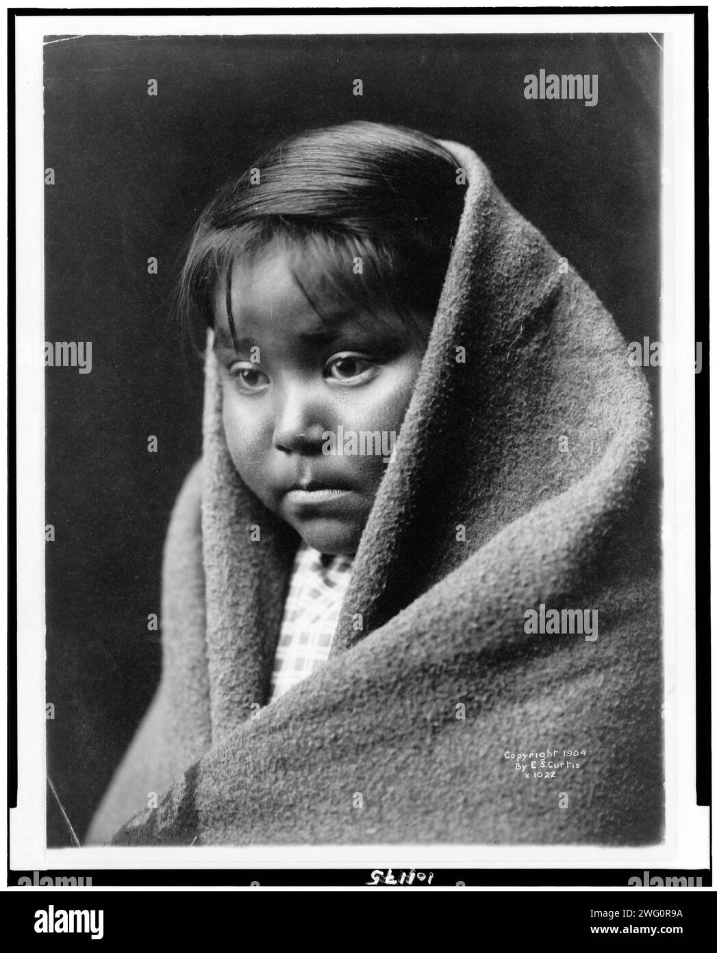 Un bambino del deserto, c1904. Ritratto della testa e delle spalle di un bambino indiano Navajo, rivolto verso la parte anteriore, coperta intorno alla parte posteriore della testa e delle spalle. Foto Stock