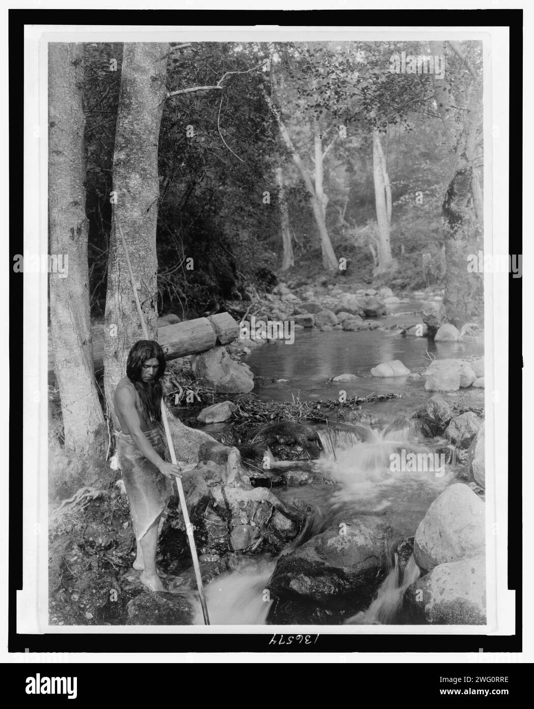 La corrente di salmone, c1923. La fotografia mostra l'uomo che tiene una lancia mentre si trova in piedi sulle rocce vicino a un ruscello in corsa. Foto Stock La corrente di salmone, c1923. La fotografia mostra l'uomo che tiene una lancia mentre si trova in piedi sulle rocce vicino a un ruscello in corsa. Foto Stock