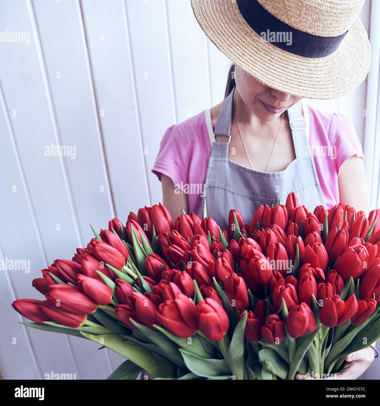 Immagine quadrata di una donna irriconoscibile che regge un grande bouquet di tulipani rossi con uno spazio per le copie. Giardiniere che indossa un cappello, un grembiule e tiene in mano splendidi fiori. Foto Stock