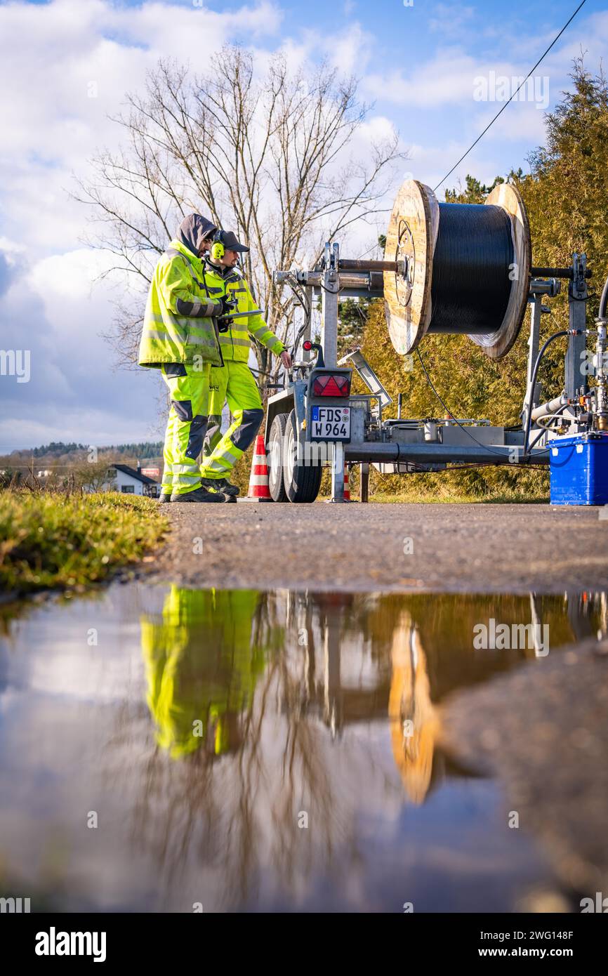 Lavoratore che ispeziona un avvolgicavo vicino a una piscina riflettente d'acqua, costruzione in fibra ottica, Nagold, Foresta Nera, Germania Foto Stock