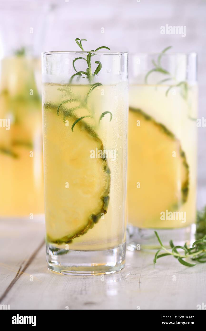 Un bicchiere di limonata con pezzi di ananas, cubetti di ghiaccio e rosmarino. Rinfresco cocktail biologico senza alcool. Foto Stock