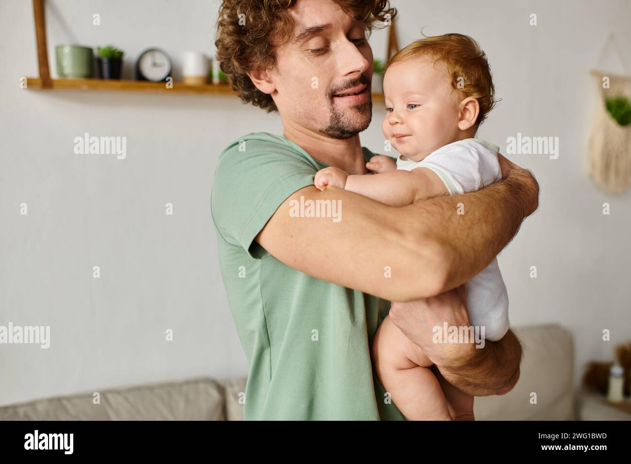 padre allegro con la barba in braccio suo figlio sorridente in un accogliente salotto, ritratto Foto Stock