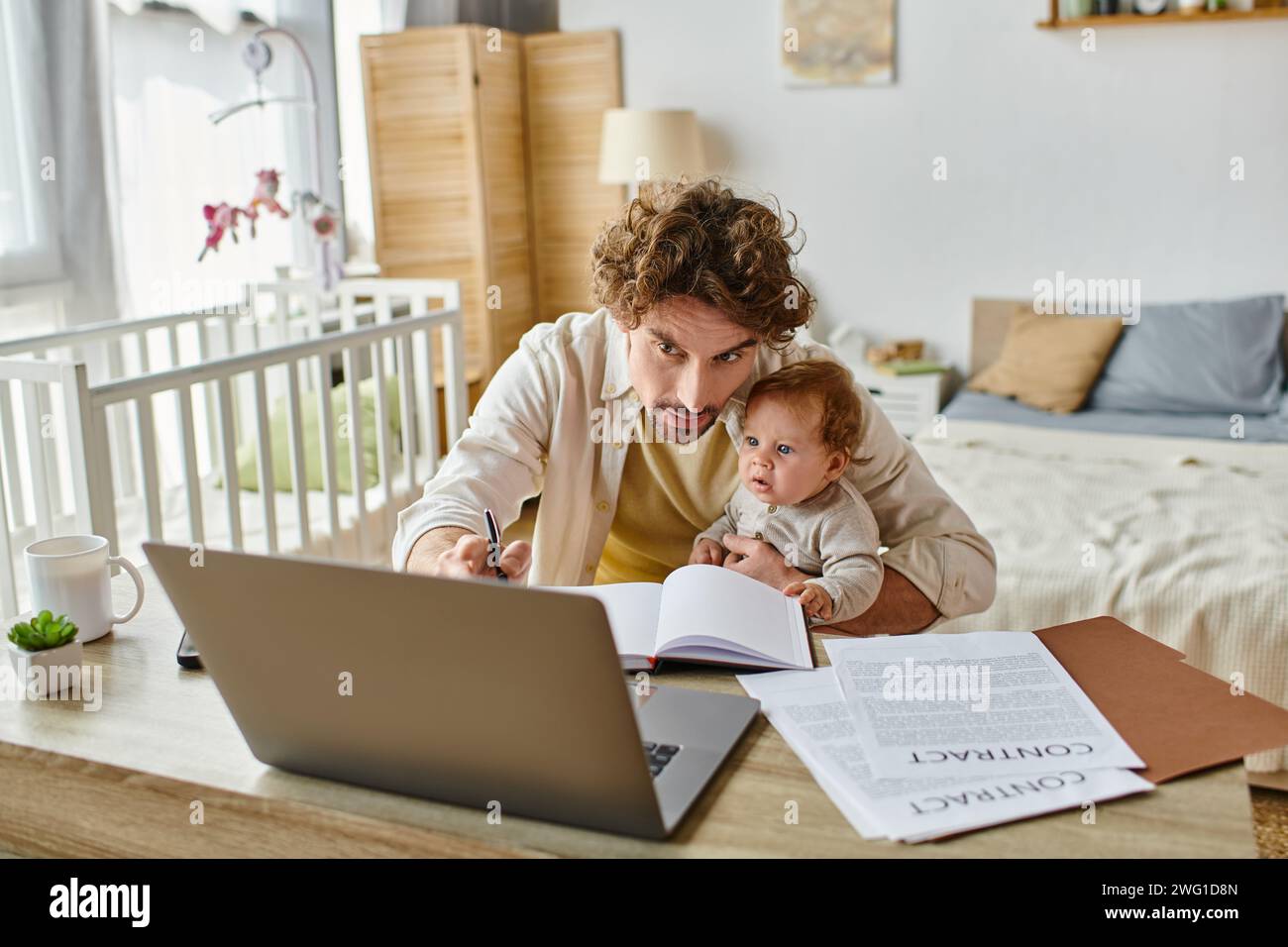 uomo che tiene in braccio il figlio neonato mentre prende appunti e lavora da casa, equilibrio tra lavoro e vita privata Foto Stock