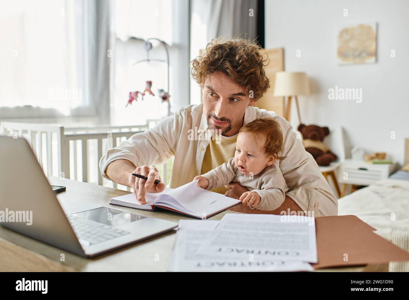 uomo che tiene in braccio il figlio neonato mentre lavora a distanza con un notebook da casa, equilibrio tra lavoro e vita privata Foto Stock
