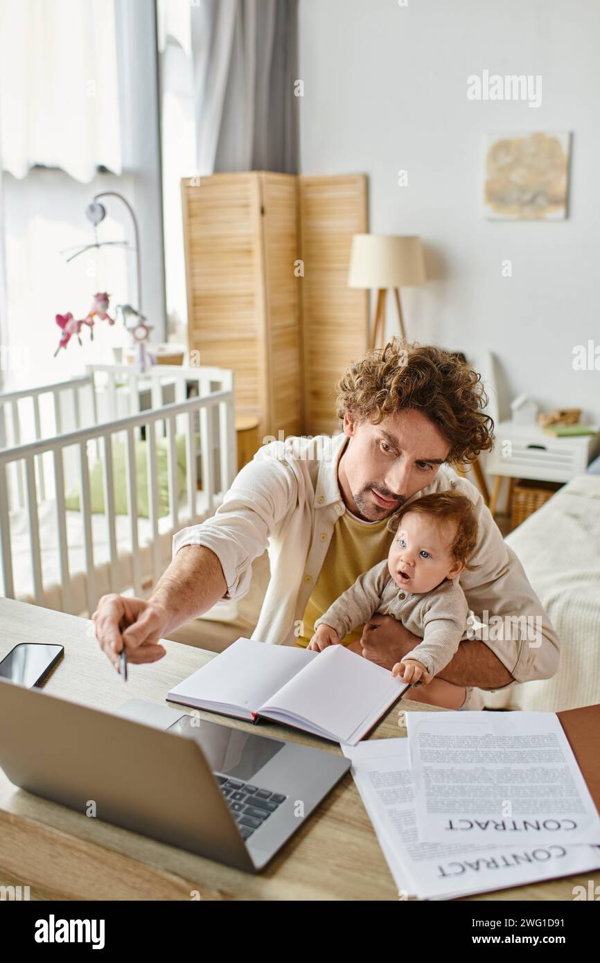 padre che tiene in braccio il figlio neonato mentre lavora a distanza su un notebook da casa, equilibrio tra lavoro e vita privata Foto Stock