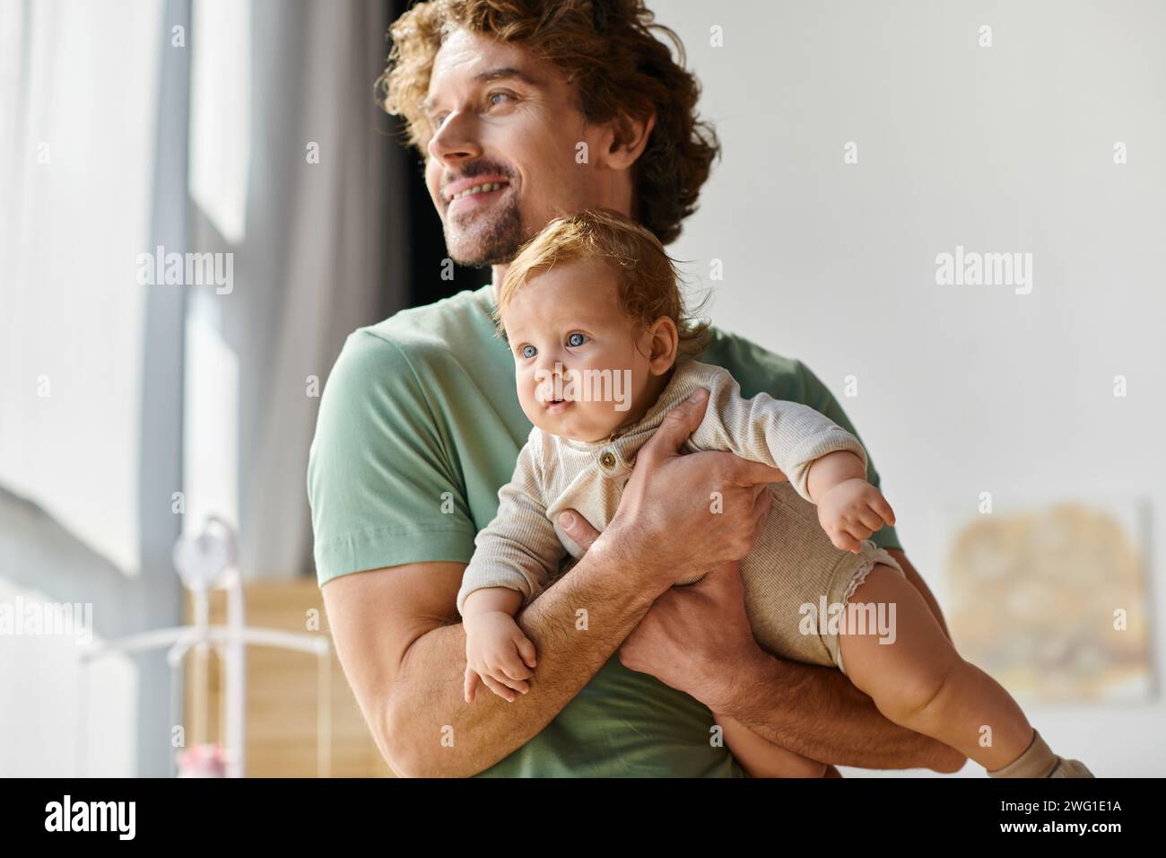 i capelli ricci e il padre felice che tiene in braccio il suo figlio neonato in una camera da letto accogliente a casa, paternità Foto Stock