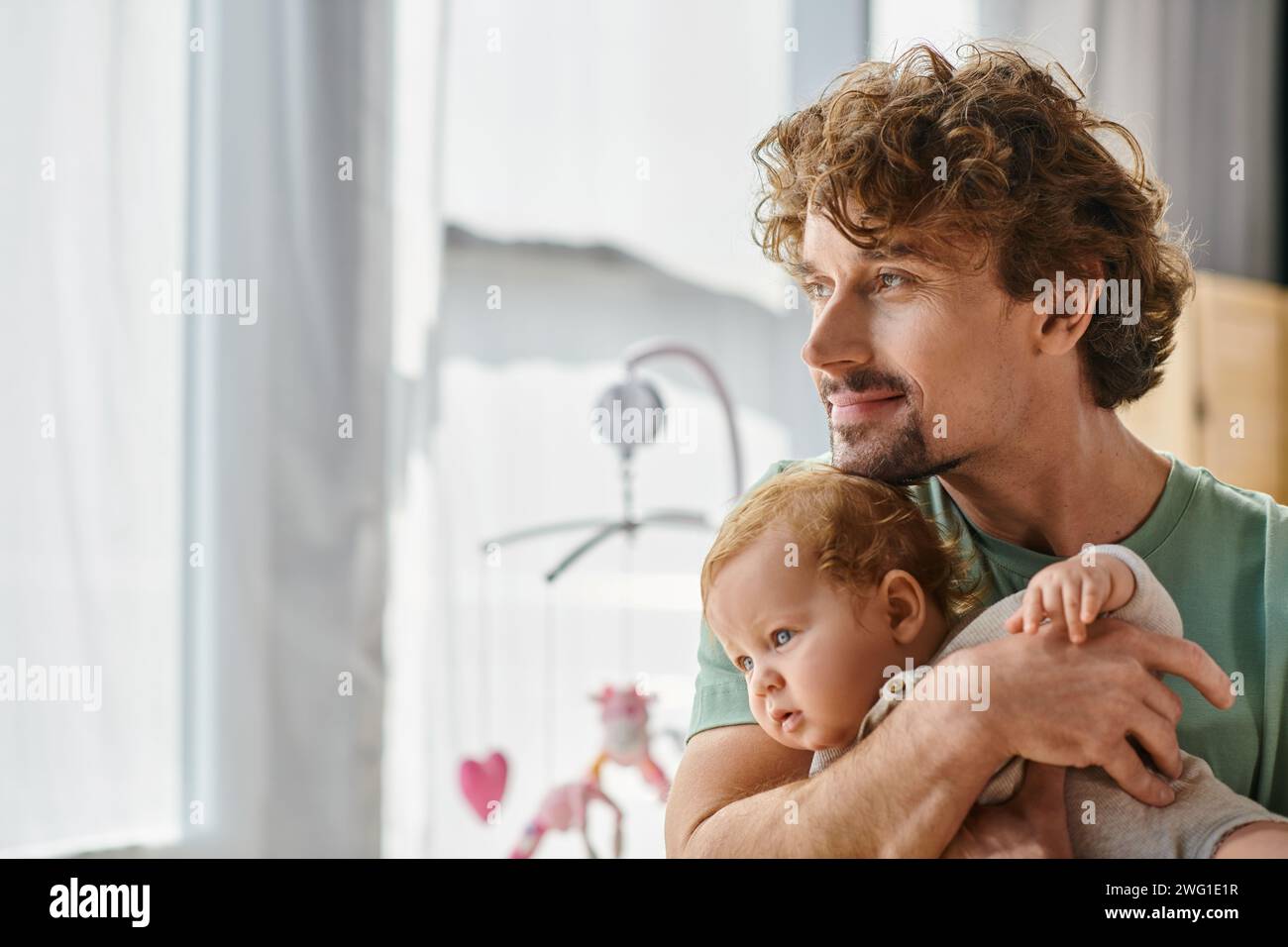 i capelli ricci e il padre felice che tiene in braccio il suo bambino in una camera da letto accogliente a casa, paternità Foto Stock