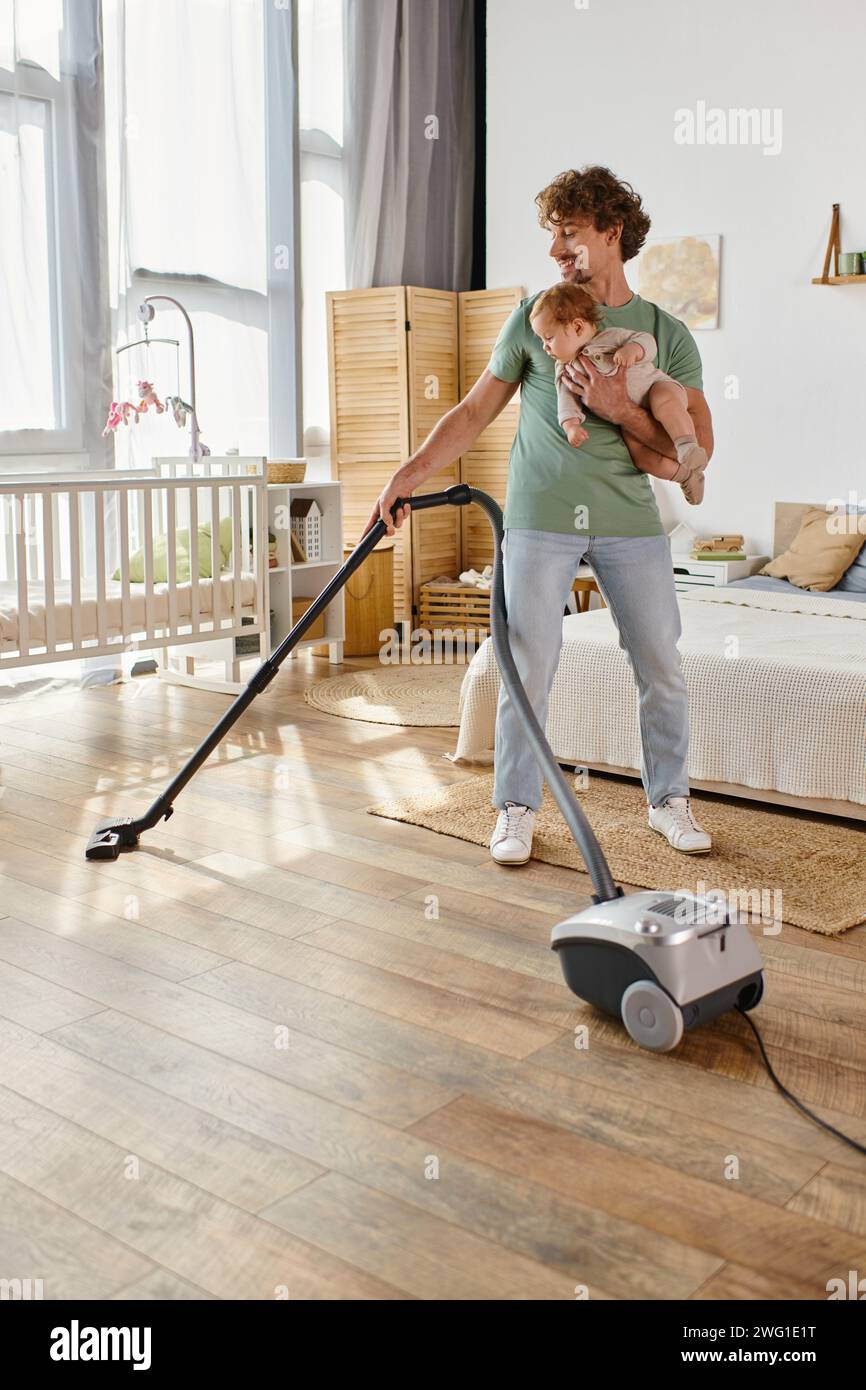 padre riccio, lavoro domestico e assistenza all'infanzia, uomo che aspira la camera da letto con il figlio in braccio Foto Stock