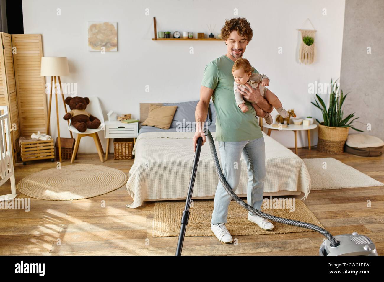 uomo felice, lavoro domestico e assistenza all'infanzia, padre che aspira la camera da letto con figlio in braccio Foto Stock