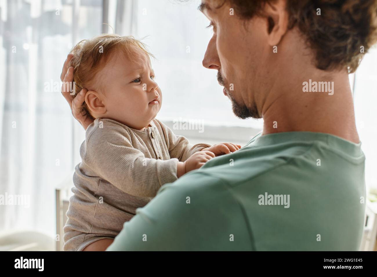 padre premuroso con capelli ricci e barba che tiene tra le braccia il suo bambino in abiti da bambino, ritratto Foto Stock