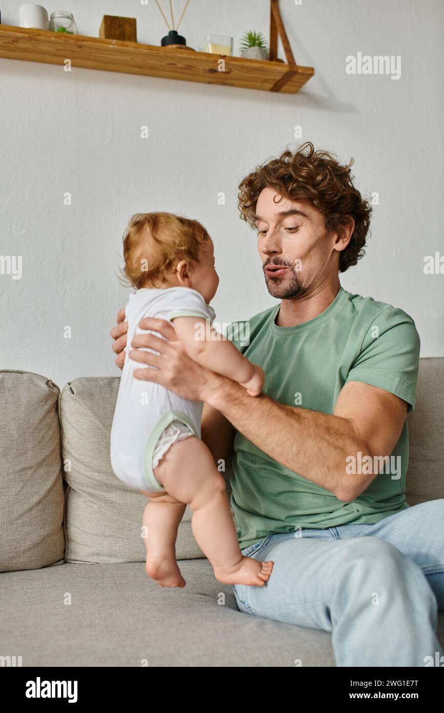 padre che tiene in braccio un bambino carino e che ha un momento felice sul divano in salotto Foto Stock