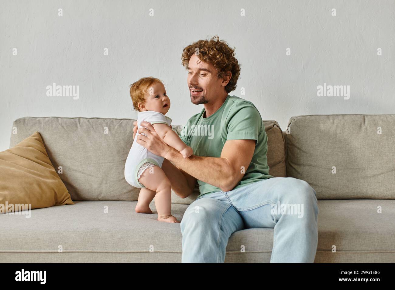 padre che tiene in braccio il suo bambino a piedi nudi e passa del tempo di qualità in salotto Foto Stock