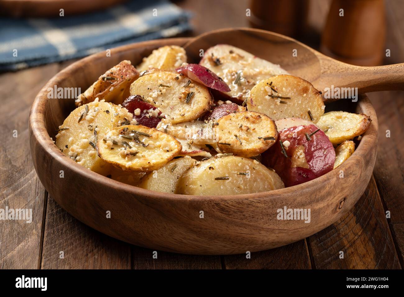 Patate arrostite a fette condite con rosmarino e aglio in un recipiente di legno su un tavolo rustico Foto Stock