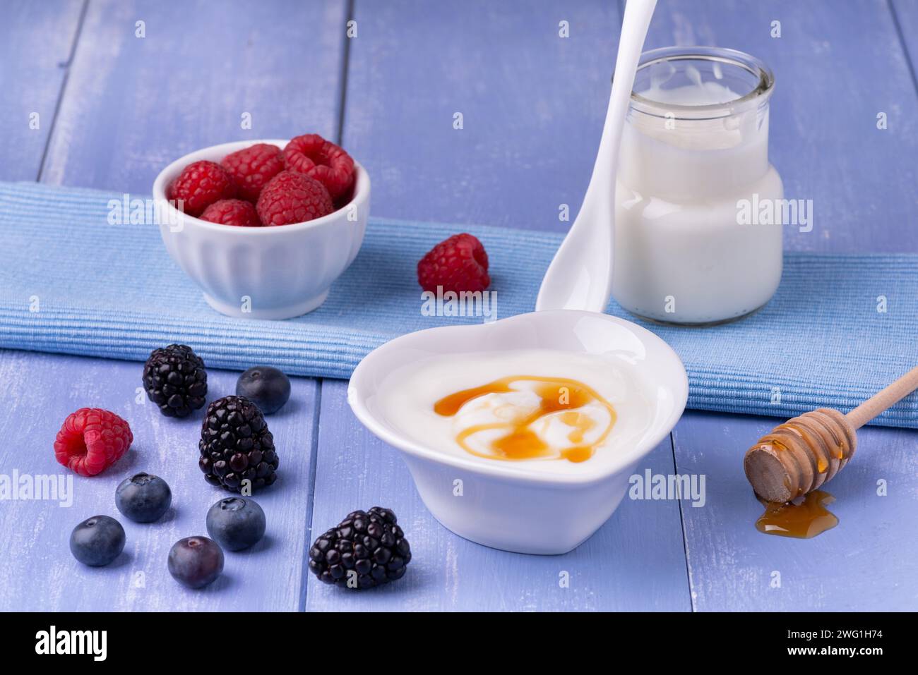 colazione. Sul tavolo di legno blu lavanda, in primo piano il recipiente con lo yogurt magro, oltre al miele biologico, il vaso di yogurt e. Foto Stock