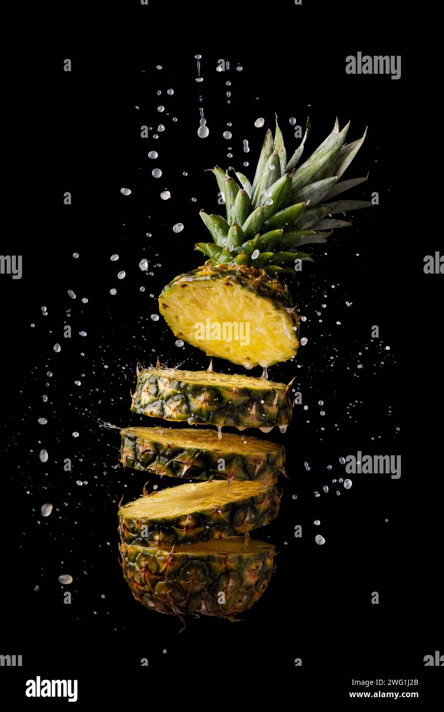 ananas fresco e tagliato a fette con schizzi di succo su sfondo nero Foto Stock