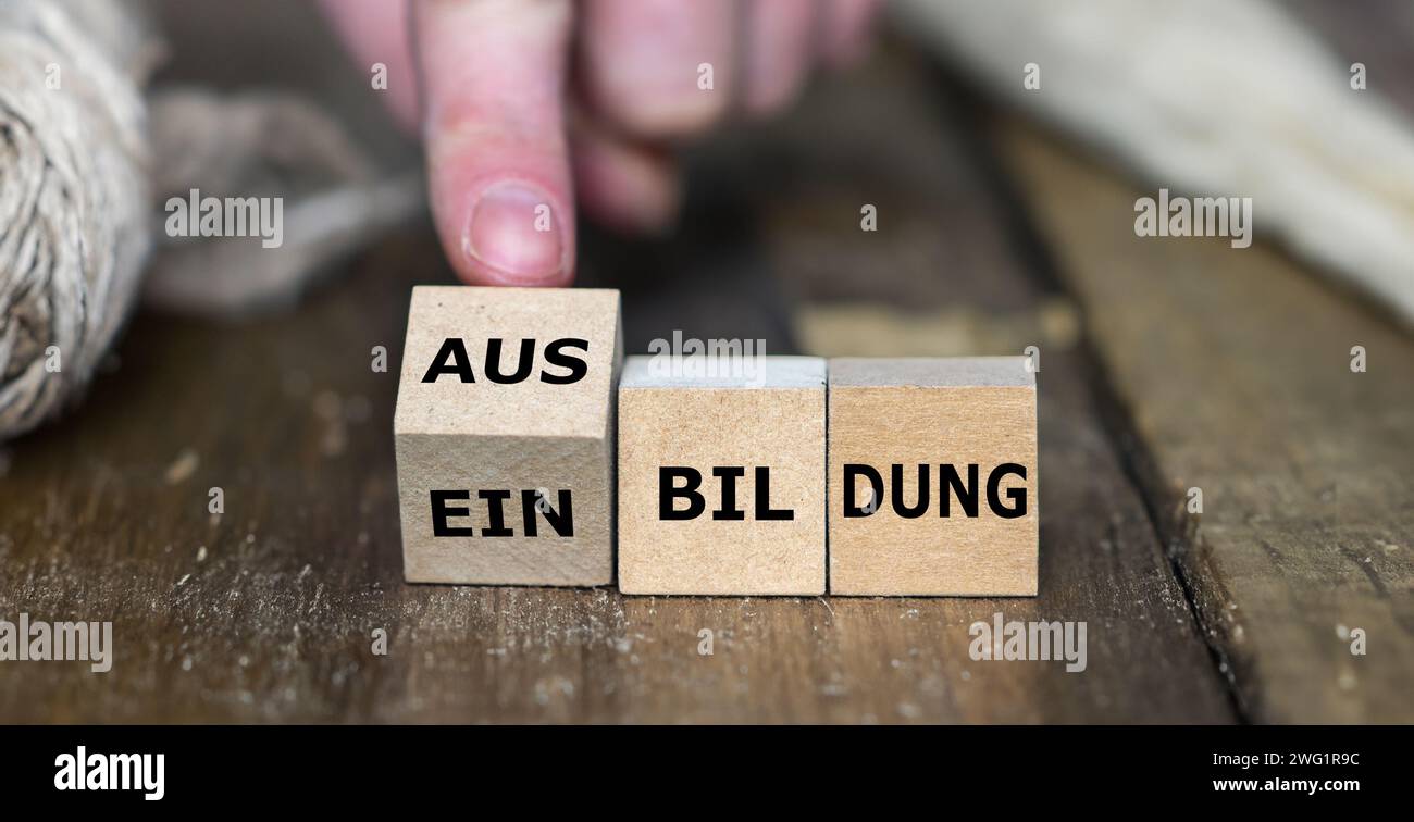 La mano trasforma il cubo di legno e cambia la parola tedesca "Einbildung" (presunzione) in "Ausbildung" (apprendistato). Foto Stock