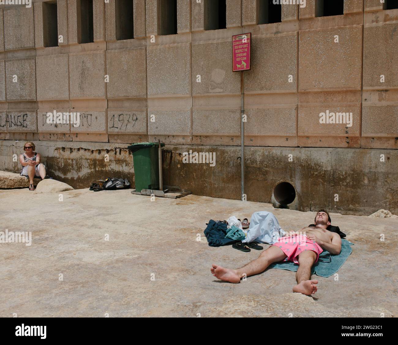 Un bagnante che indossa pantaloncini rosa può essere visto dormire e prendere il sole sulle rocce di Tigne Point a Malta. Foto Stock