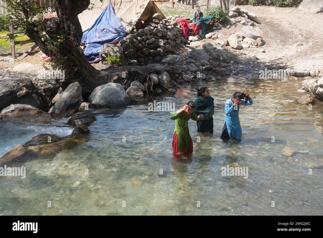 Una vivace scena fluviale a Sarkegad, un villaggio rurale di montagna nepalese a Humla. Le donne nepalesi in abito tradizionale si lavano nel fiume. Foto Stock