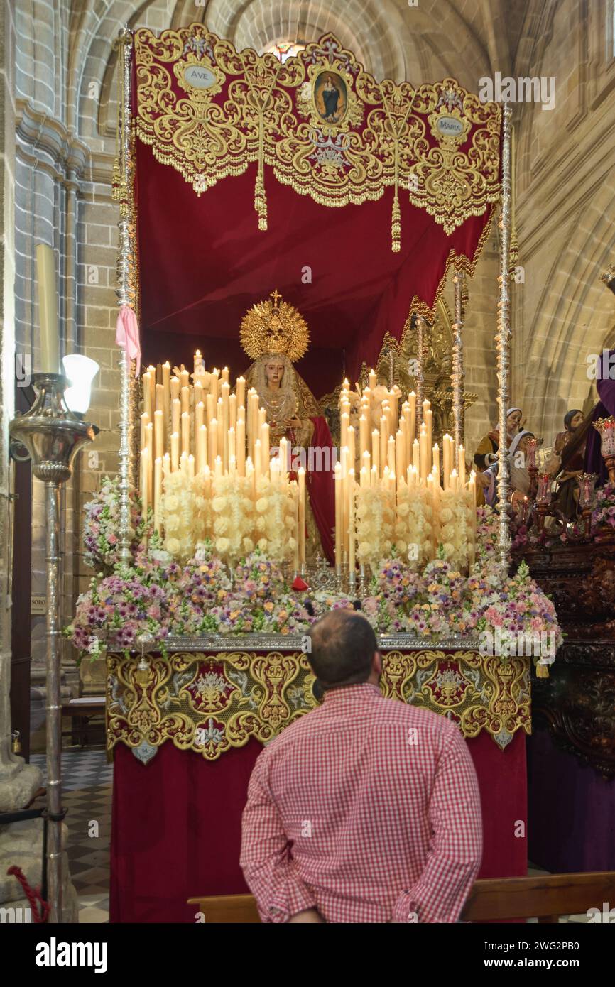 Jerez de la Frontera, Spagna - 01 febbraio 2024: Uomo con grande devozione di fronte ad un passaggio della settimana Santa in Spagna con la Vergine circondata da illuminata ca Foto Stock