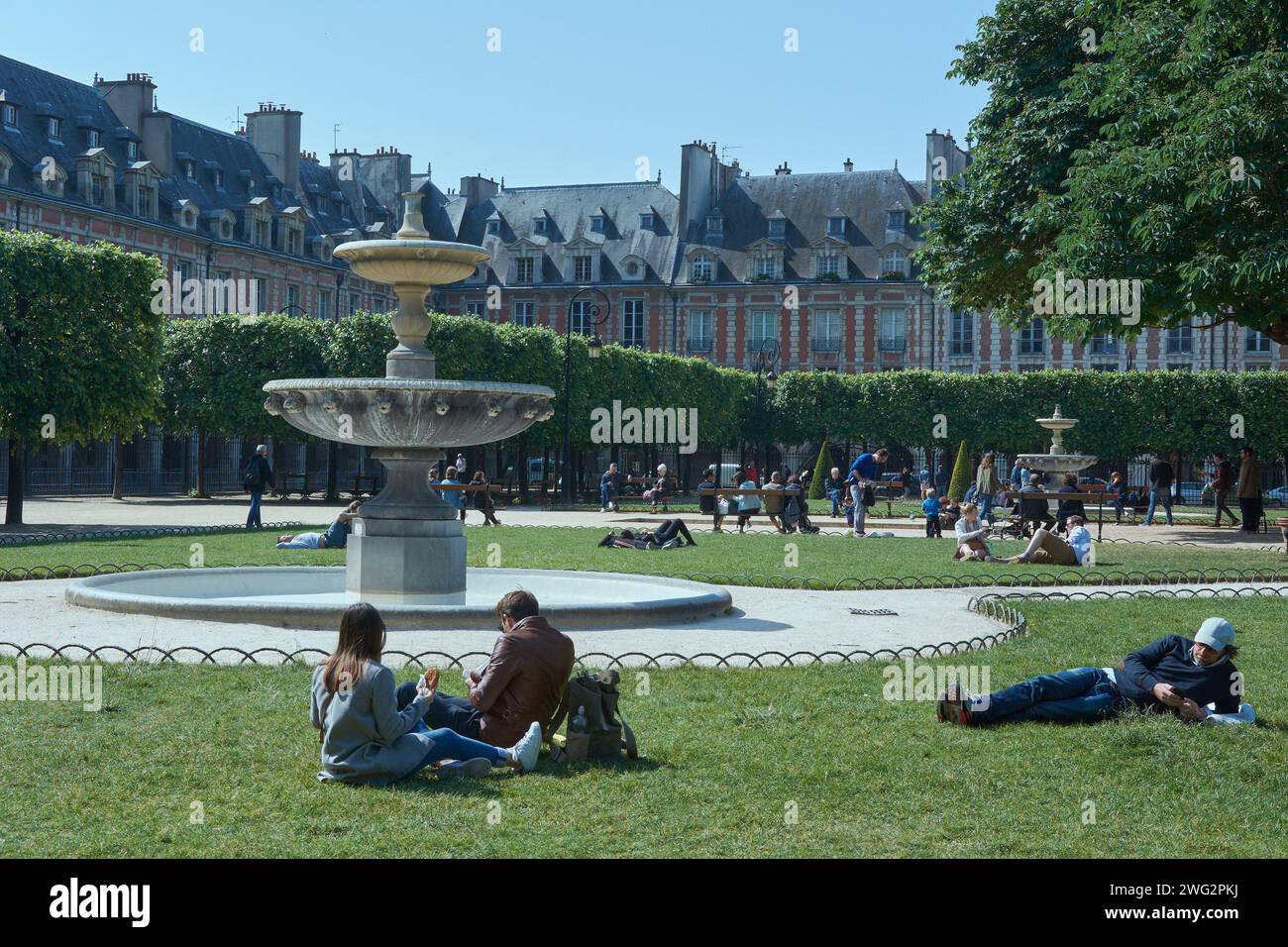 Gruppo di persone che si godono l'atmosfera tranquilla del parco, accompagnati da una fontana accattivante e da un paesaggio urbano sullo sfondo Foto Stock