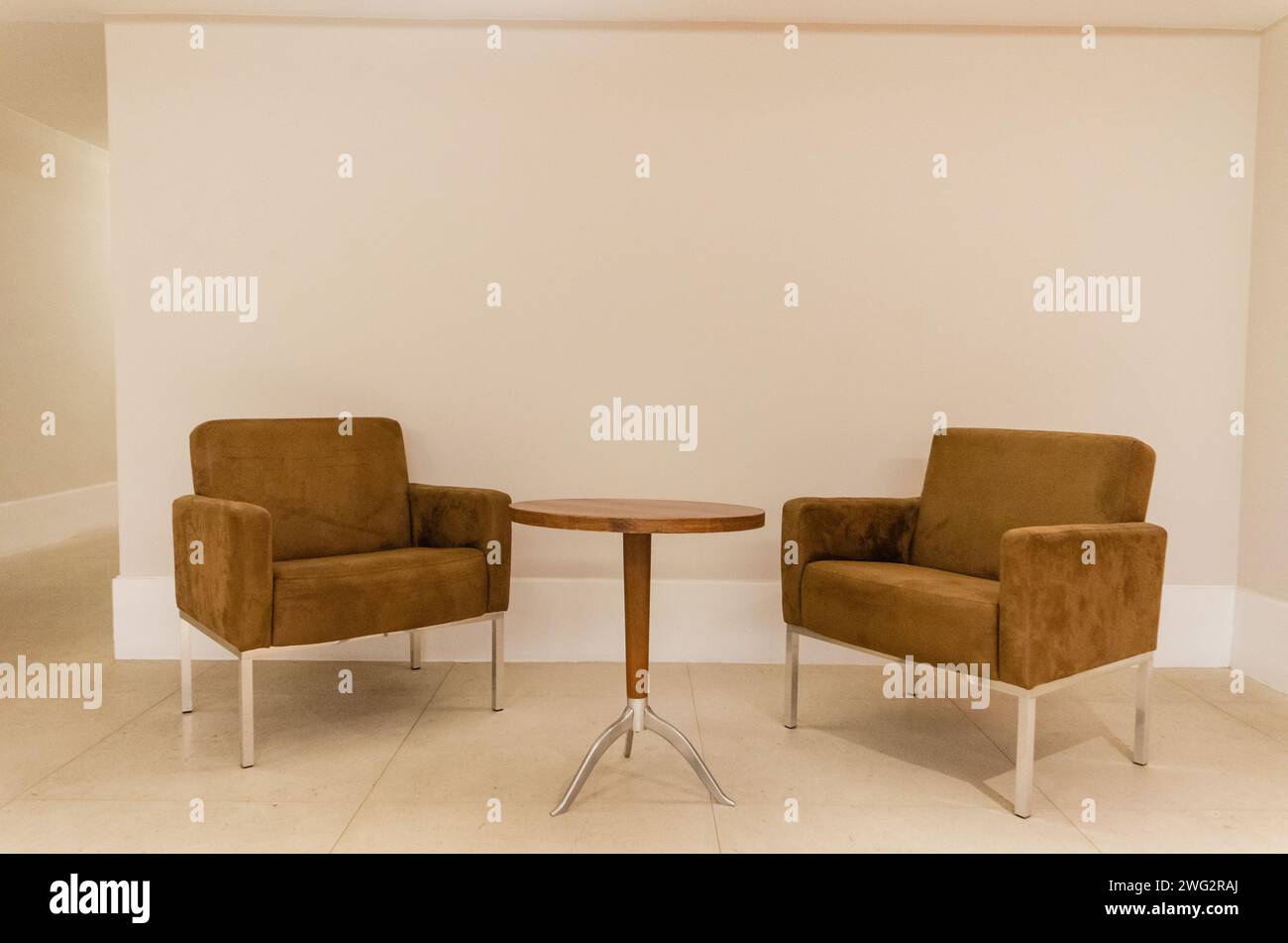 Due sedie marroni e un tavolo contro una parete bianca in una stanza Foto Stock