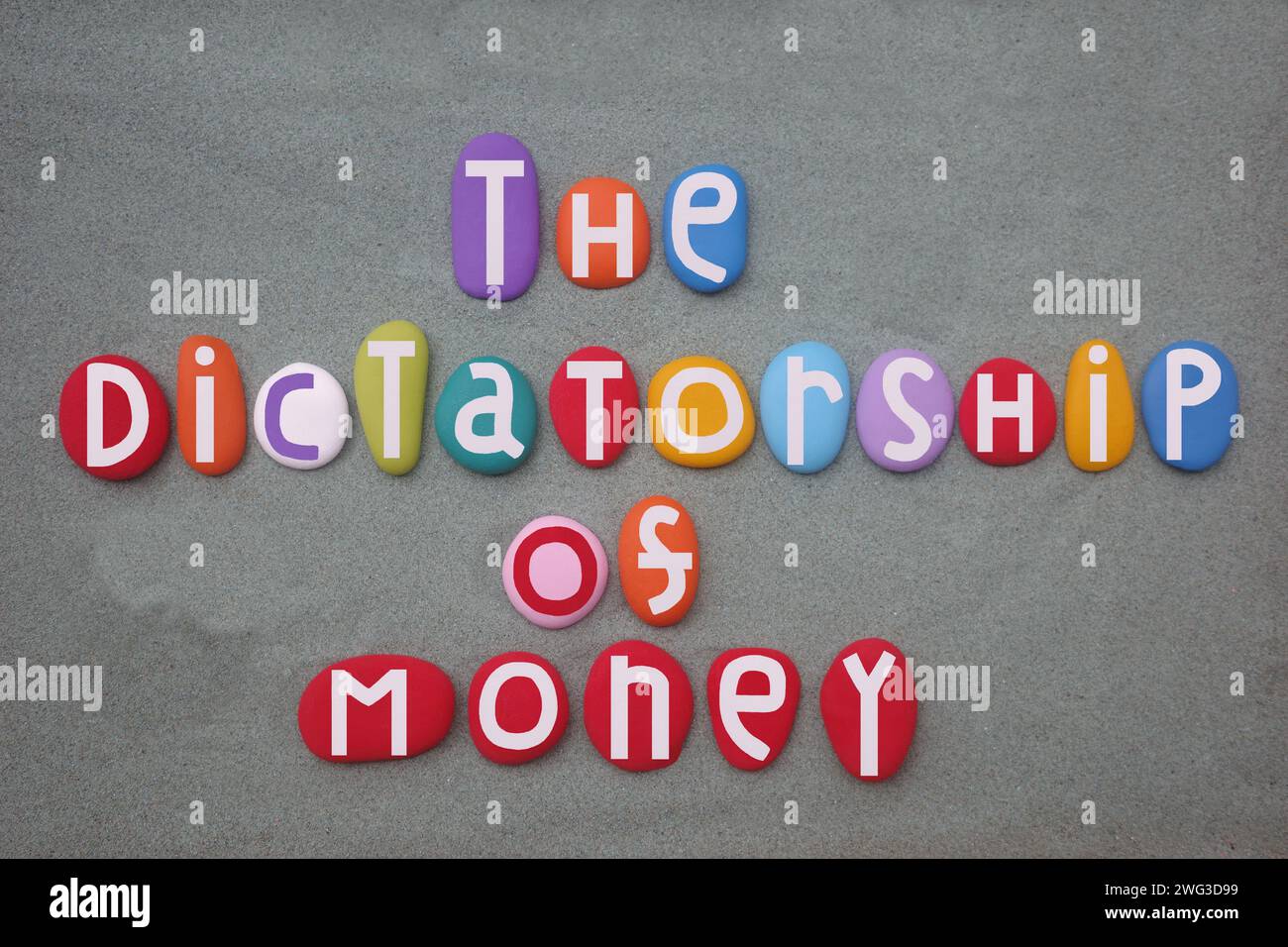 La dittatura del denaro, slogan sociale composto da lettere di pietra colorate dipinte a mano su sabbia verde Foto Stock