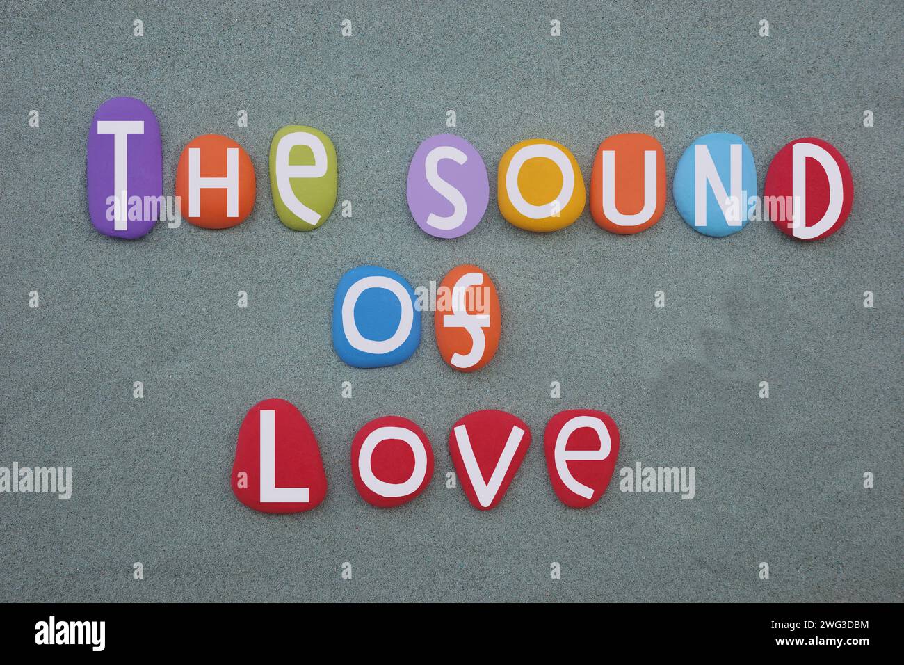 Il suono dell'amore, slogan creativo composto da lettere in pietra multicolore dipinte a mano su sabbia verde Foto Stock