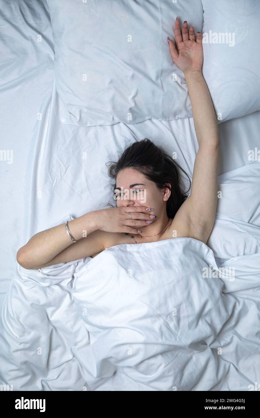 Una bella ragazza dorme in un letto con una lenzuola bianche Foto Stock