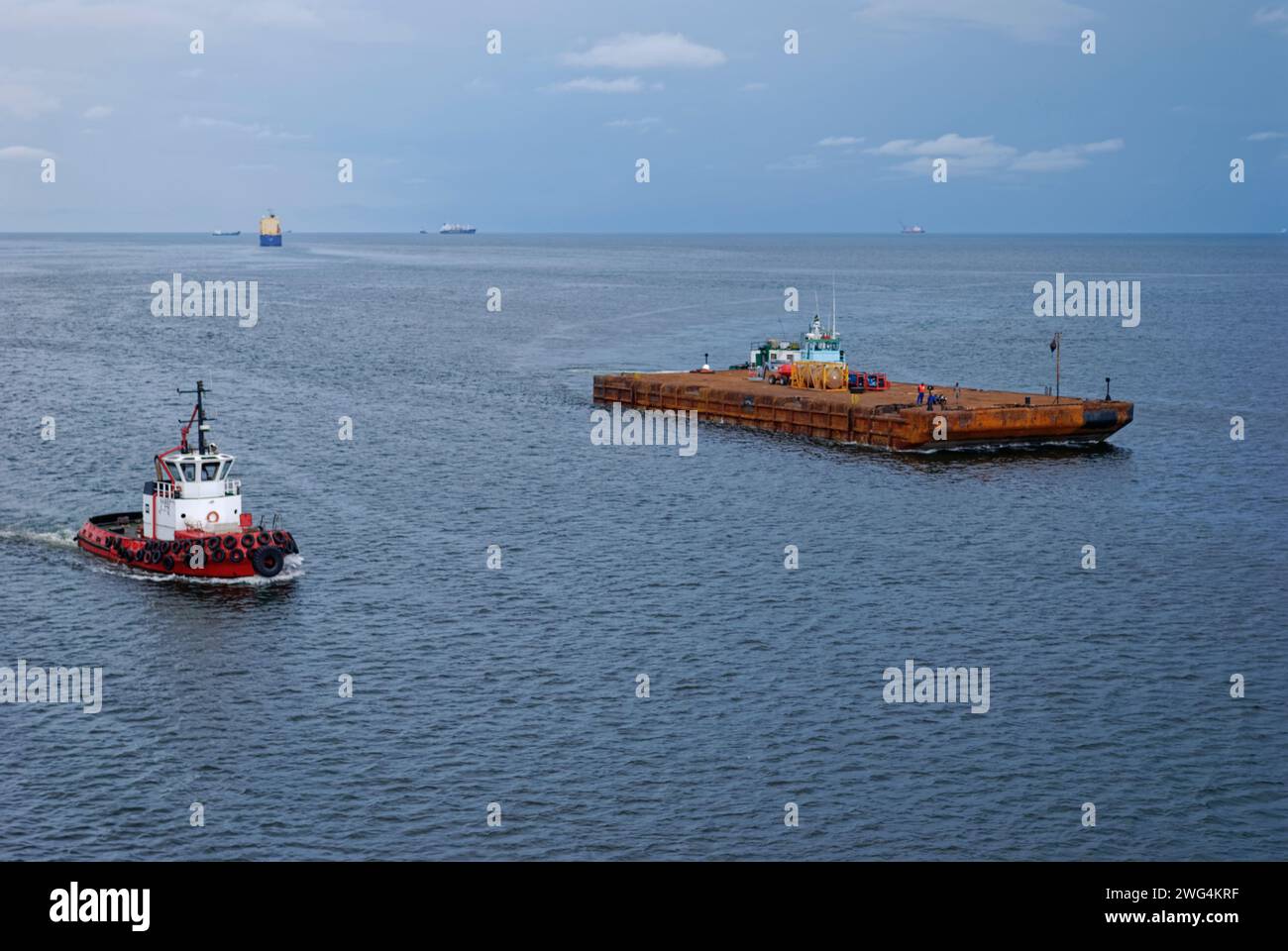 Una chiatta galleggiante in corso nella baia di Cap Lopez a Port Gentil, scortata da un Tug Boat pronto ad assistervi quando raggiunge la sua destinazione. Foto Stock