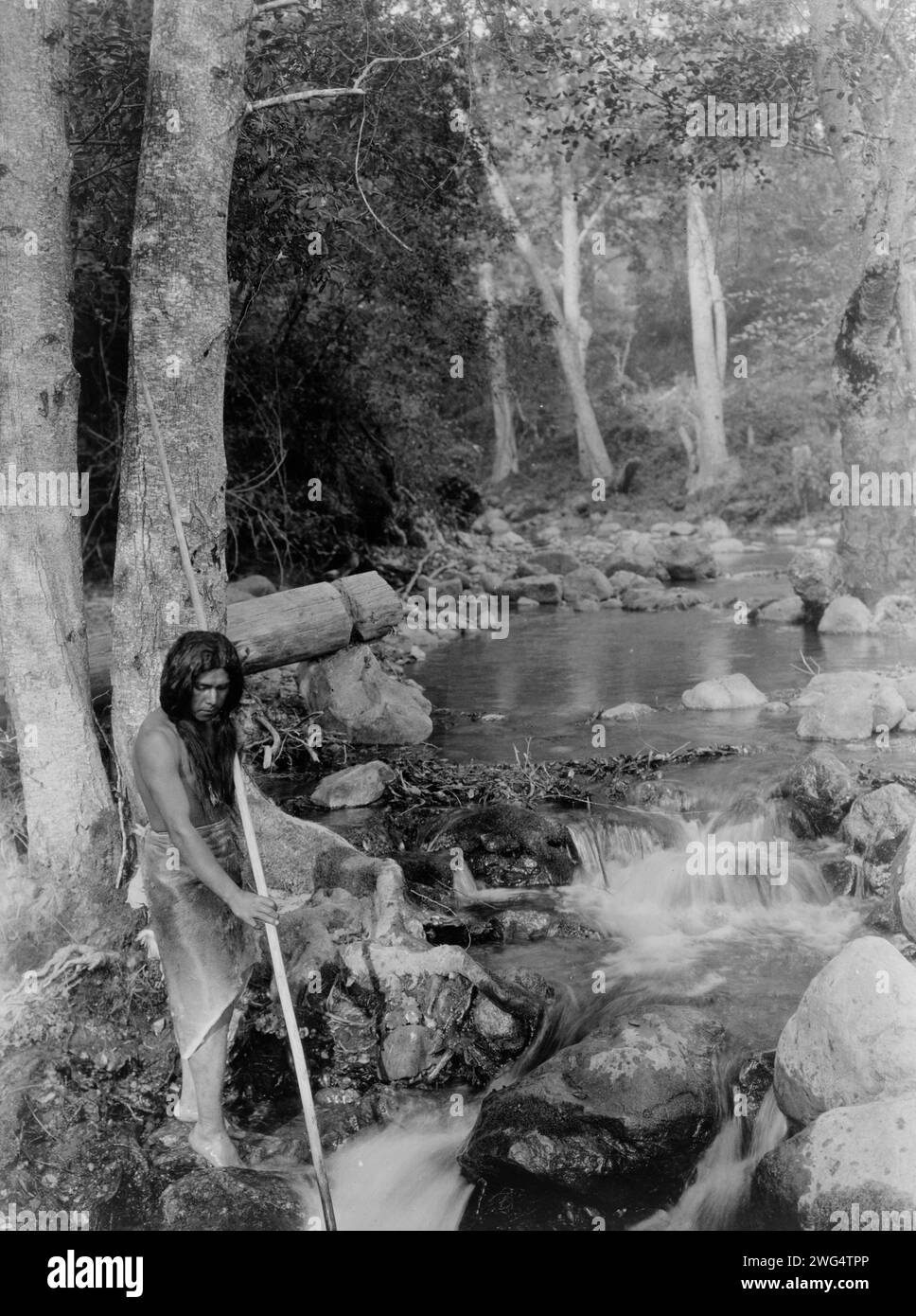 La corrente di salmone, c1923. La fotografia mostra l'uomo che tiene una lancia mentre si trova in piedi sulle rocce vicino a un ruscello in corsa. Foto Stock La corrente di salmone, c1923. La fotografia mostra l'uomo che tiene una lancia mentre si trova in piedi sulle rocce vicino a un ruscello in corsa. Foto Stock
