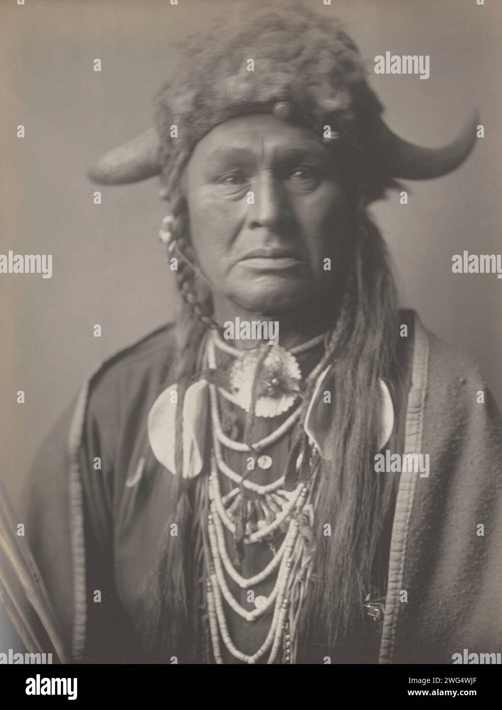 White Man lo gestisce, 1908 anni. La fotografia mostra un ritratto testa e spalle di White Man che lo guida, indossando un cappello di pelliccia con corna di bufalo, vestito in abiti tradizionali, seduto, rivolto verso la parte anteriore. Foto Stock