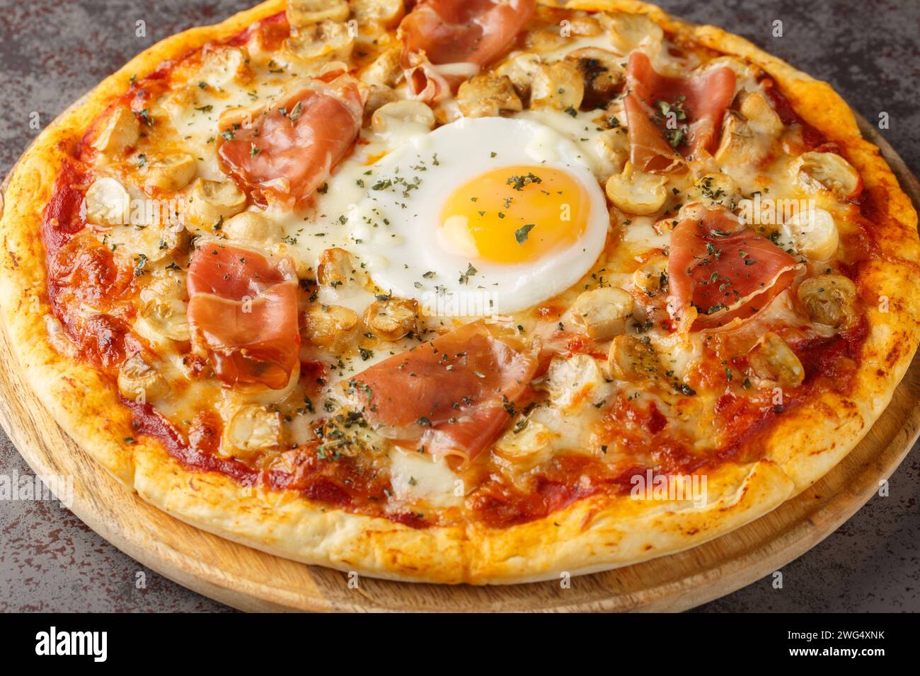 Pizza alla Bismarck un impasto base della pizza è condito con salsa di pomodoro, mozzarella, funghi, prosciutto e primo piano d'uovo sulla tavola di legno sulla linguetta Foto Stock