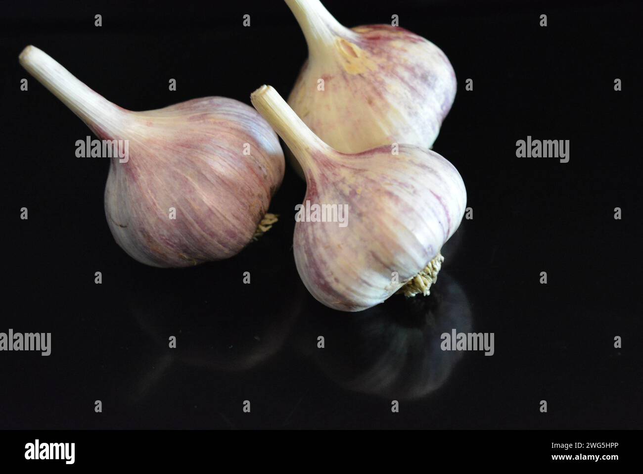 Verdure fresche, tre teste di vitello adagiate su una superficie nera lucida con riflessi ripetuti. Foto Stock