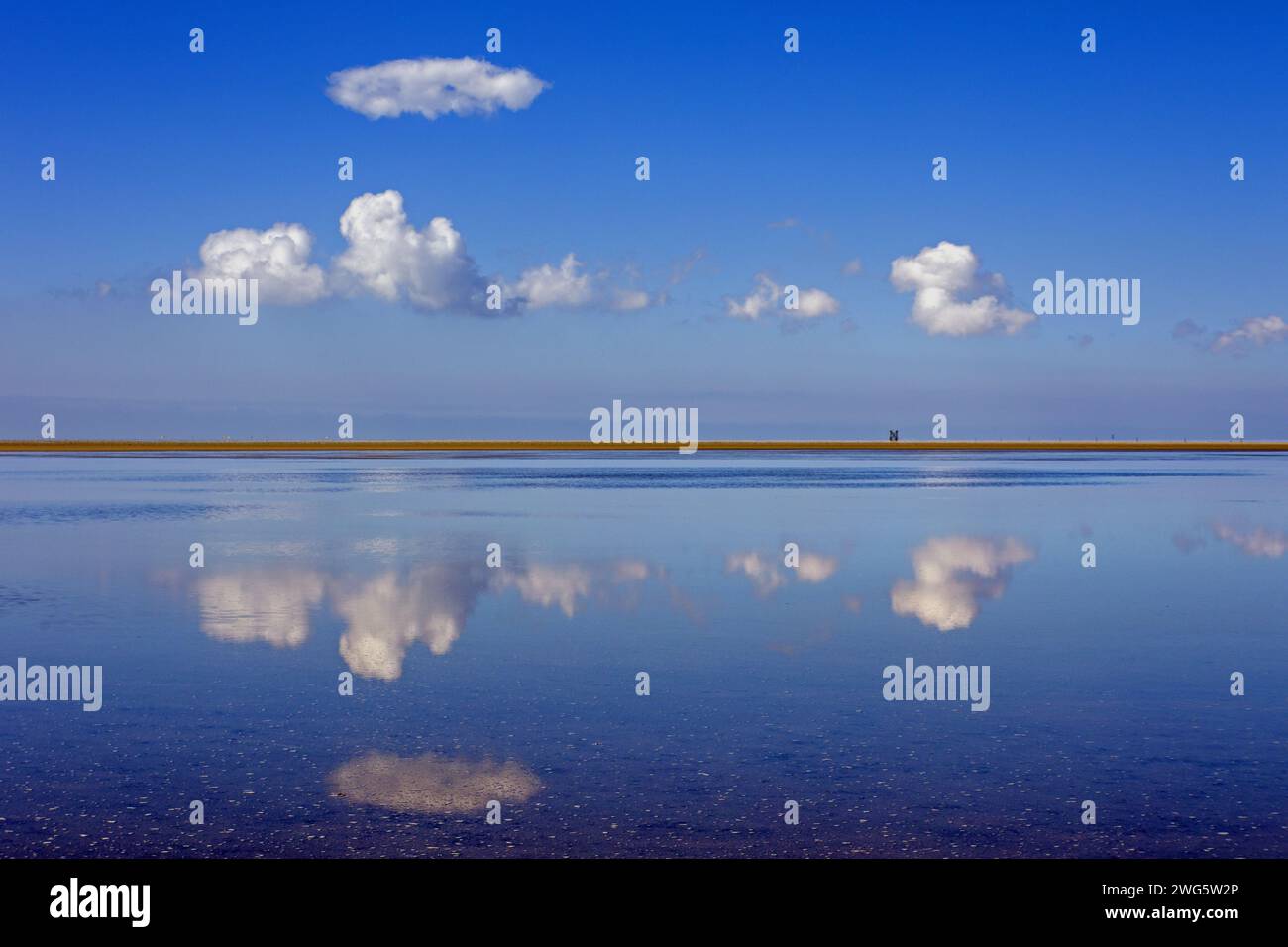 un lago liscio riflette nuvole e un cielo blu con un tratto di terra al centro Foto Stock