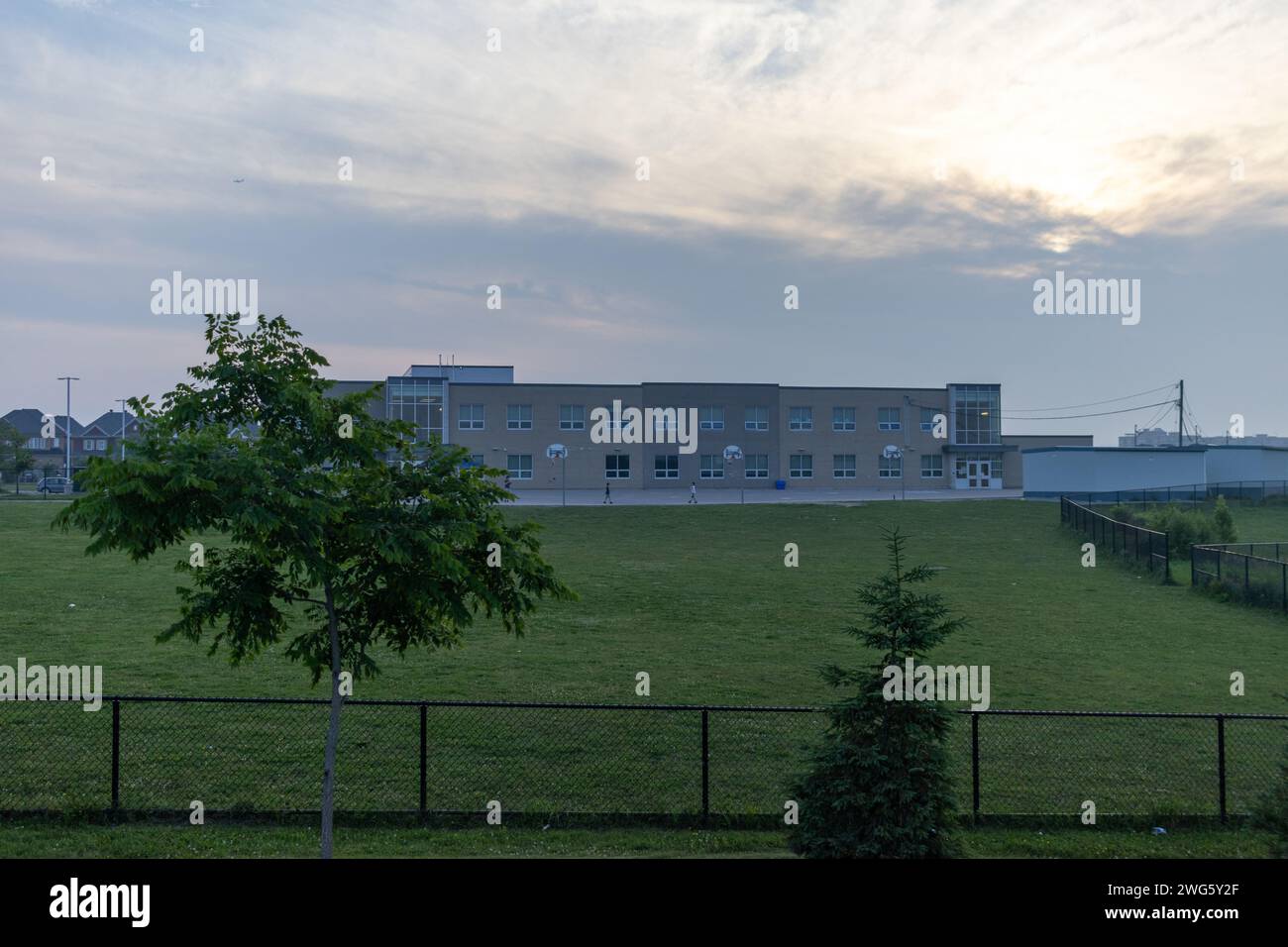 Moderno edificio scolastico - sullo sfondo di un cielo nuvoloso al crepuscolo - circondato da un prato verde ben tenuto - delimitato da una recinzione nera. Preso Foto Stock