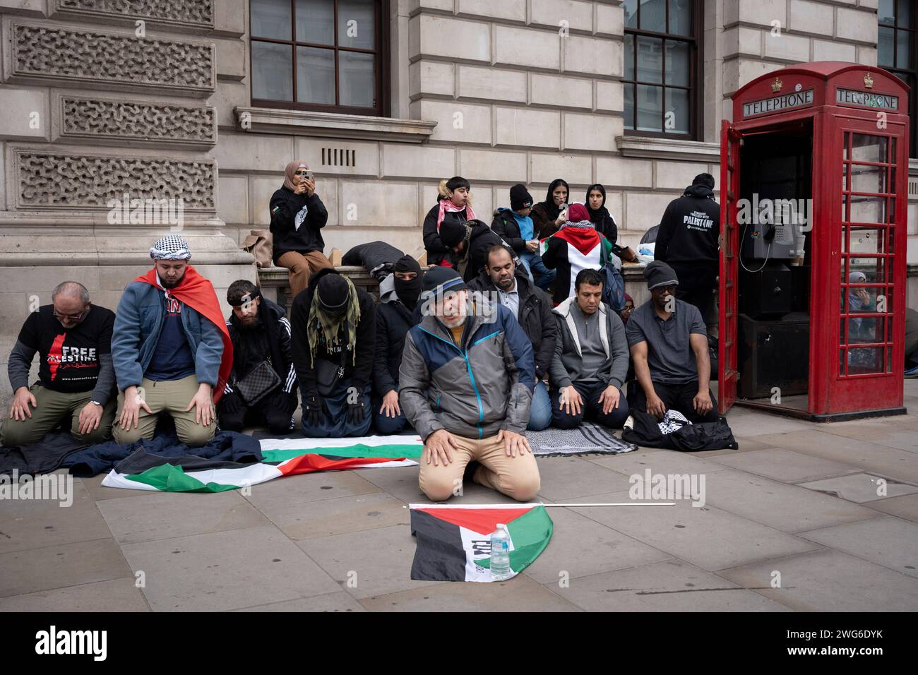 Mentre i sostenitori filo-palestinesi marciano di nuovo attraverso il centro di Londra per chiedere un cessate il fuoco permanente a Gaza, gli uomini musulmani pregano accanto a una cabina telefonica a Whitehall, il 3 febbraio 2024, a Londra, in Inghilterra. Foto Stock