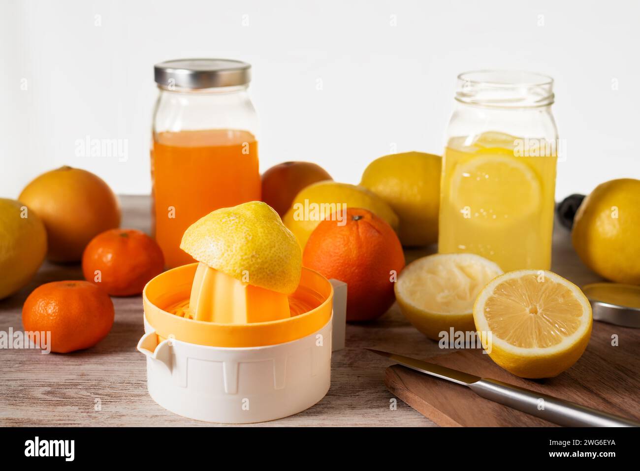 Centrifuga manuale accanto a diversi agrumi per preparare il succo, accanto a due vasetti, uno con succo d'arancia e l'altro con succo di limone. Foto Stock