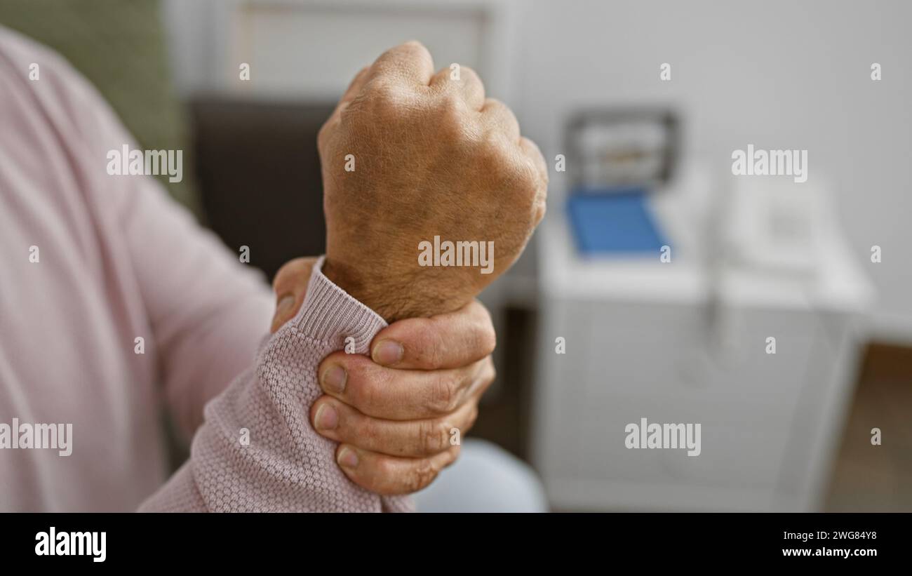 Uomo di mezza età con capelli grigi che soffre di dolore al polso a casa. Foto Stock