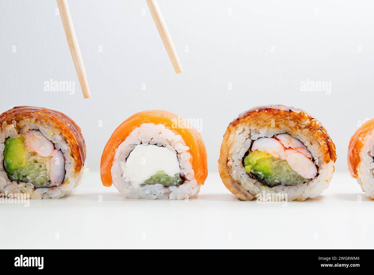 Una linea di sushi roll assortiti, tra cui involtini di avocado Philadelphia e anguille con un paio di bacchette, sorvolano sopra una selezione di sushi roll, preparati al momento Foto Stock