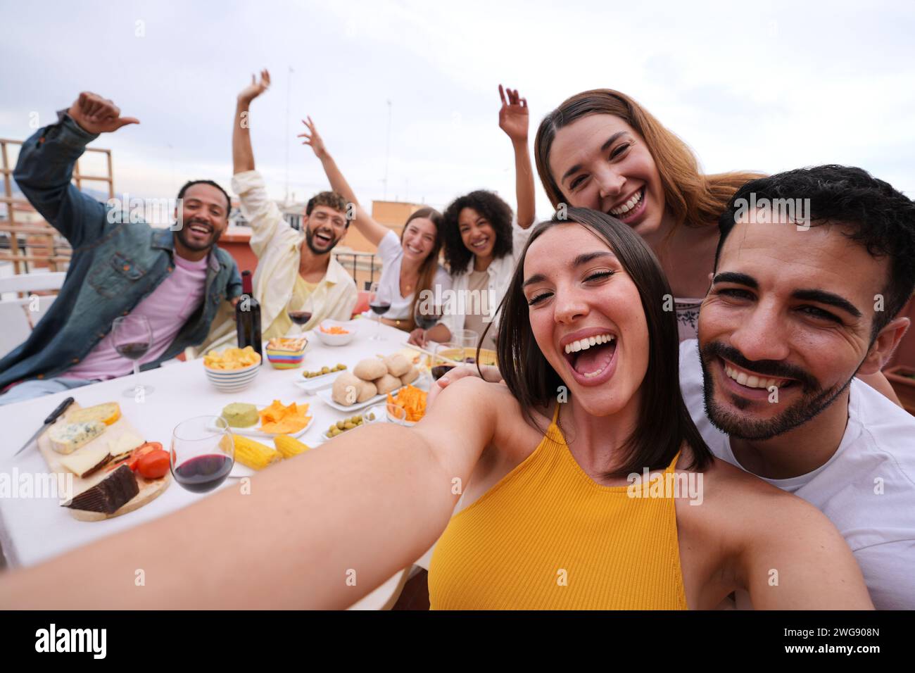 Eccitata giovane bella donna che scatta selfie di gruppo con amici gioiosi sul tetto. Foto di gente allegra Foto Stock