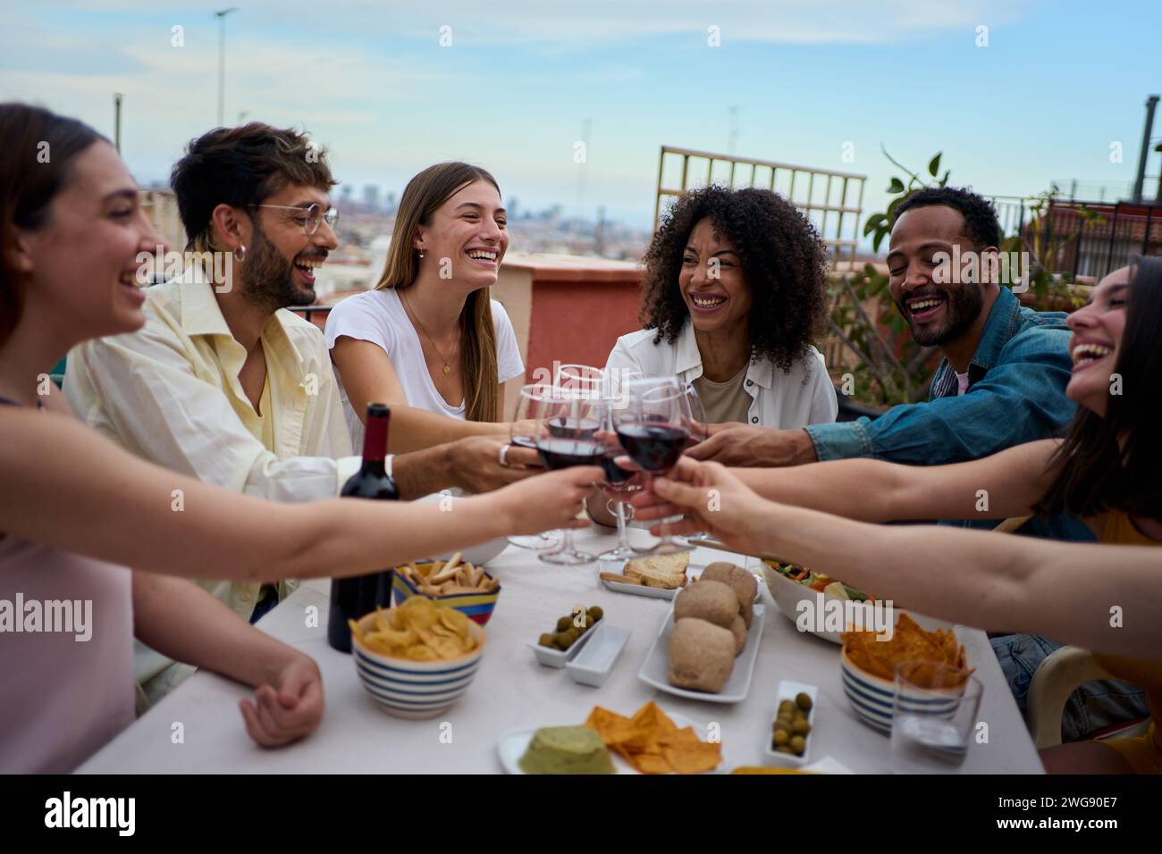 Un gruppo di giovani amici che si divertono a pranzare insieme per festeggiare il brindisi sul tetto. Foto Stock