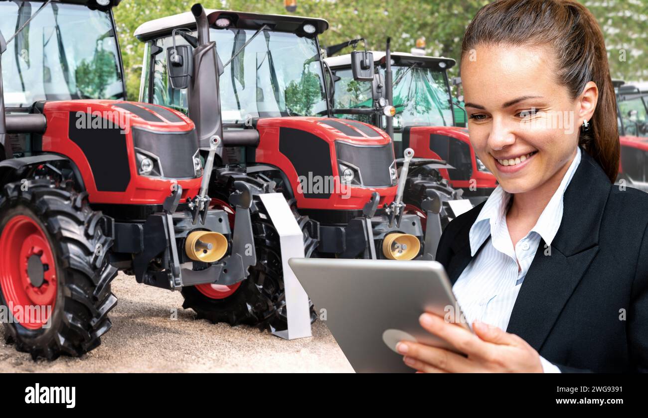 Rappresentante di vendita donna che presenta i trattori agricoli con tablet digitale. Donna d'affari di fronte ai trattori agricoli. Foto Stock