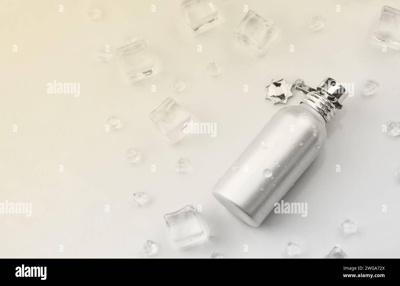 Bottiglia argentata di profumo femminile, fotografia oggettiva della bottiglia di profumo metallico in cubetti di ghiaccio e acqua su tavolo bianco. Vista dall'alto. Foto del prodotto mockup, concetto di freschezza e aroma Foto Stock